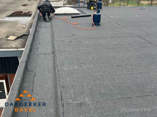 Dakdekker repareert bitumen dakbedekking op groot plat dak in Bavel Dakdekker repareert bitumen dakbedekking op groot plat dak in Bavel